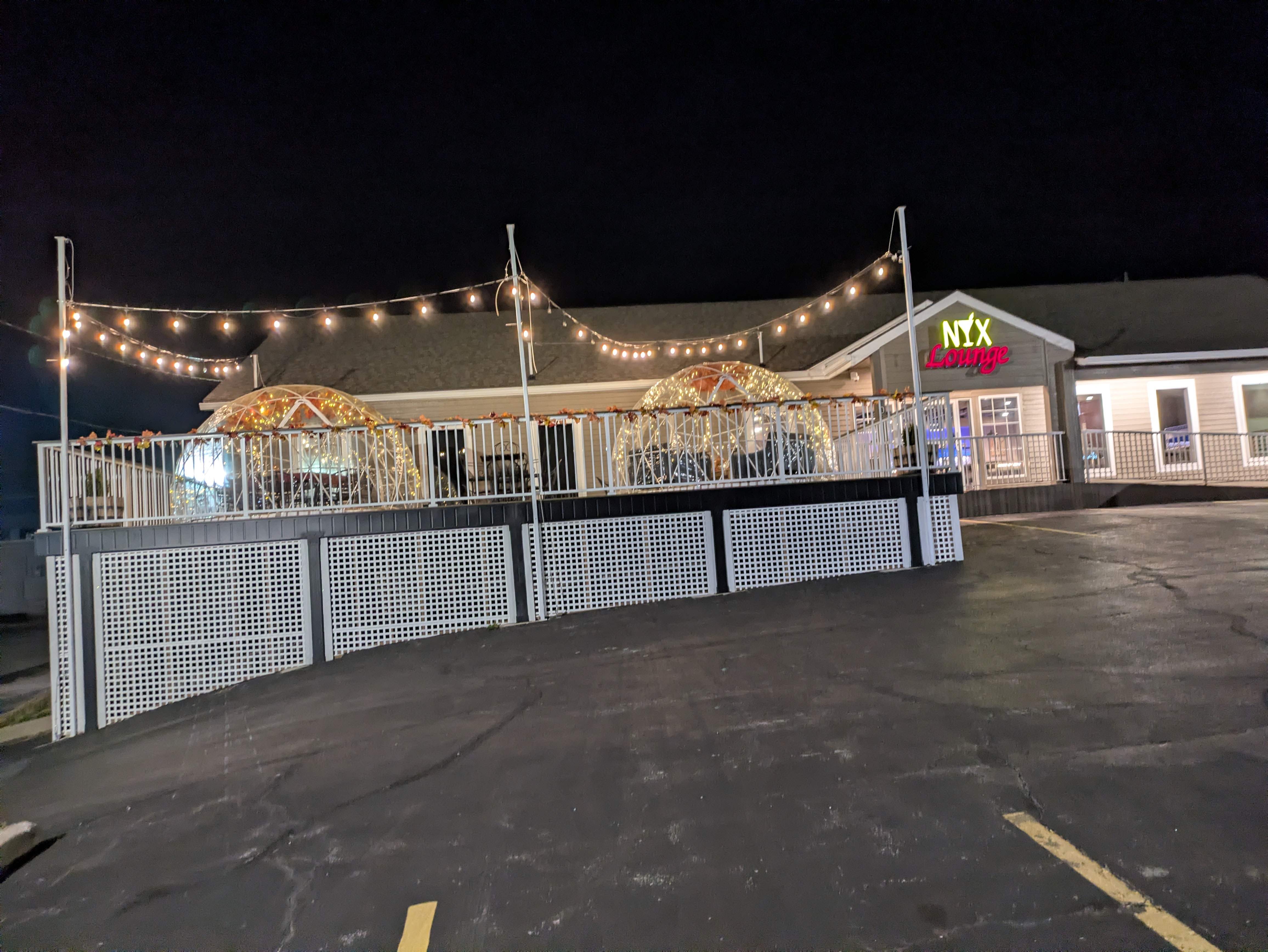 The NYX Lounge building at night with two lit igloos on the raised deck beneath string lights.