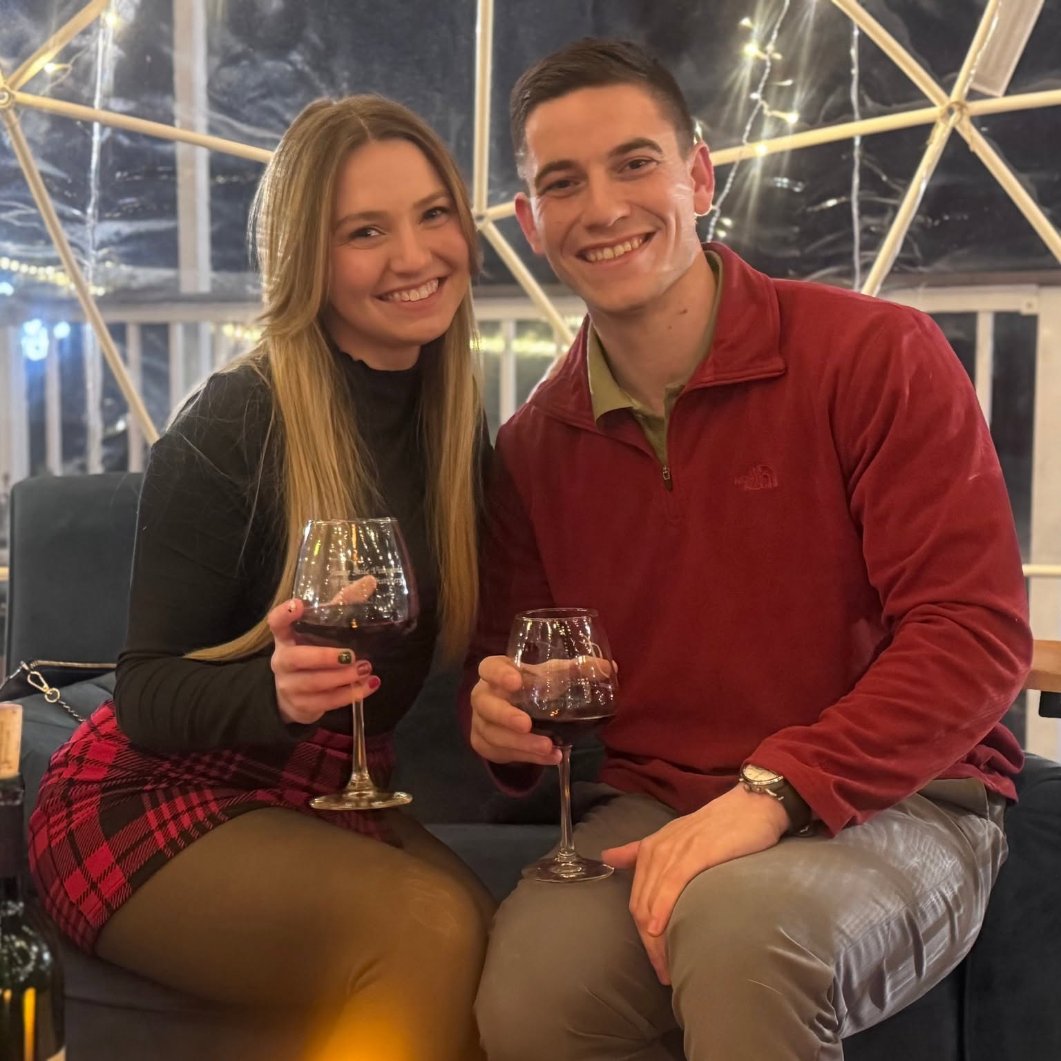 A couple smiling and holding glasses of red wine inside an NYX igloo.