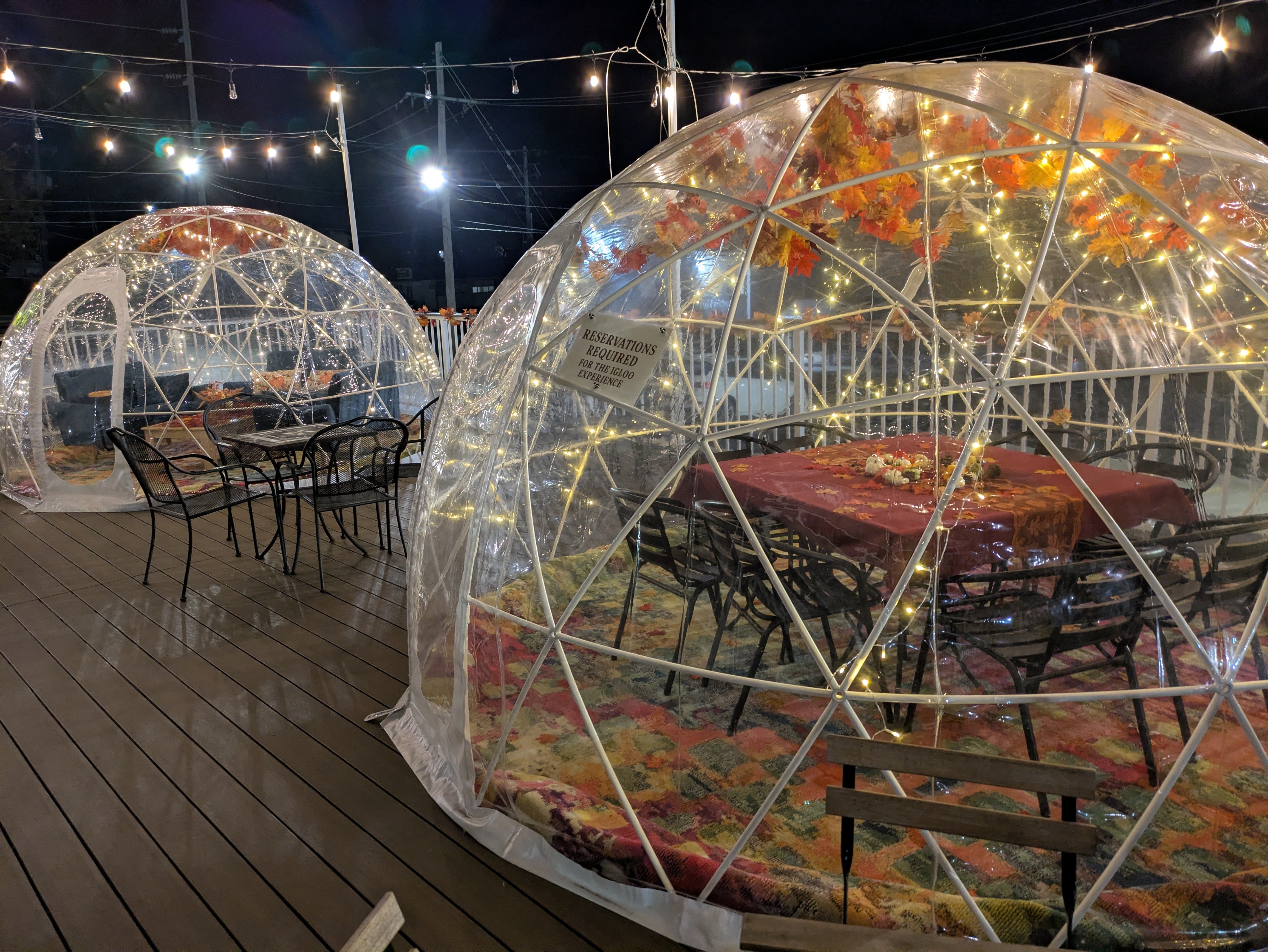 Two lit igloos on the NYX deck at night beneath strings of lights, one set up with a table and chairs.