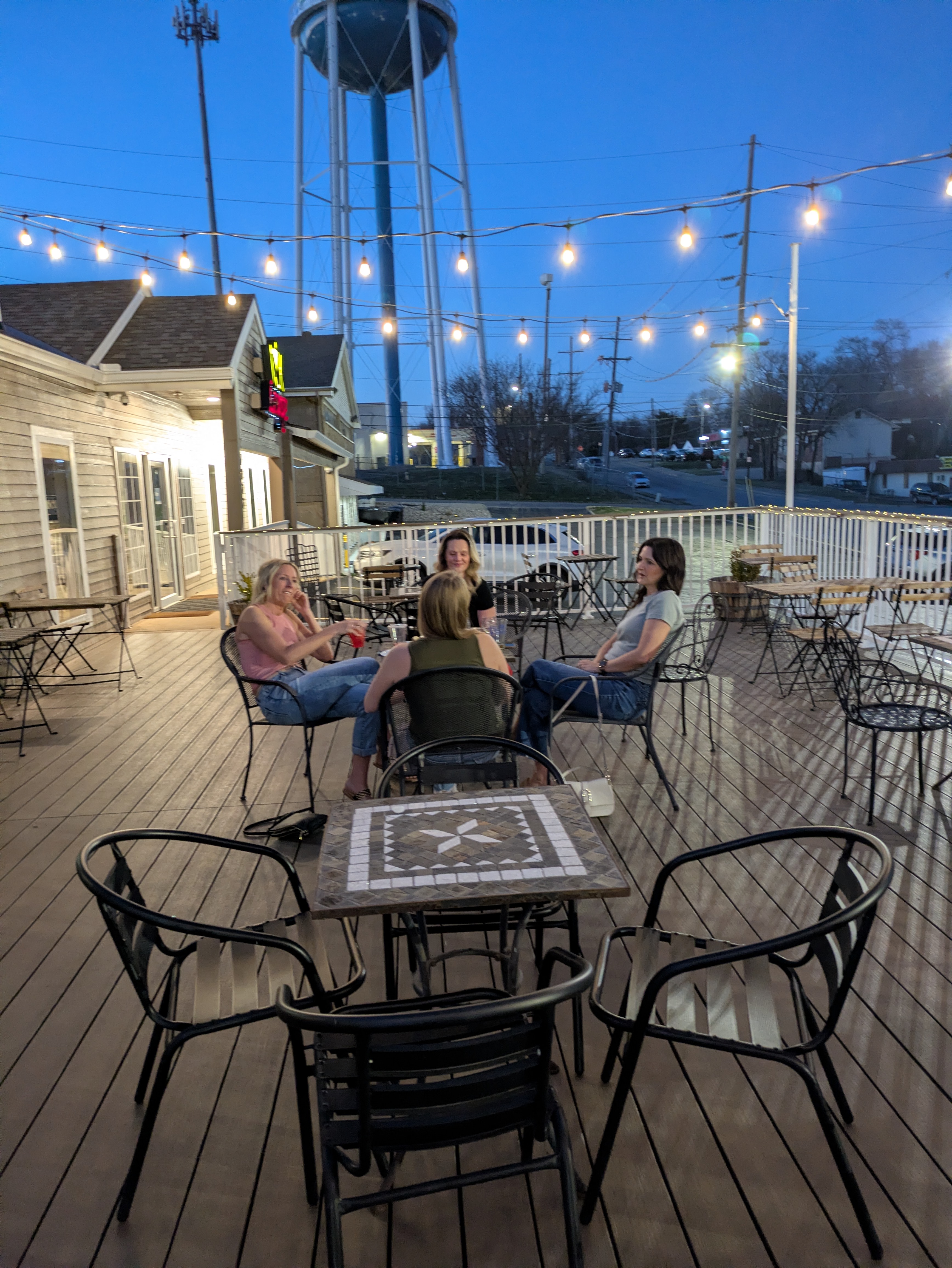 Friends on the NYX patio at night under string lights — perfect for before or after dinner in Gladstone Missouri
